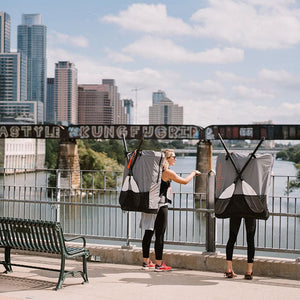 women with Oru Kayak backpacks looking over bridge