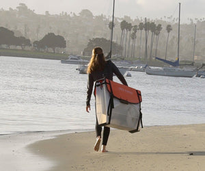 woman walking on beach carrying Oru Kayak Coast XT
