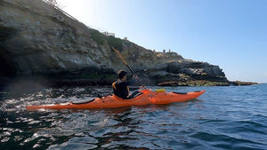 Man paddling along rocky coastline in a Pakayak Bluefin 142 kayak